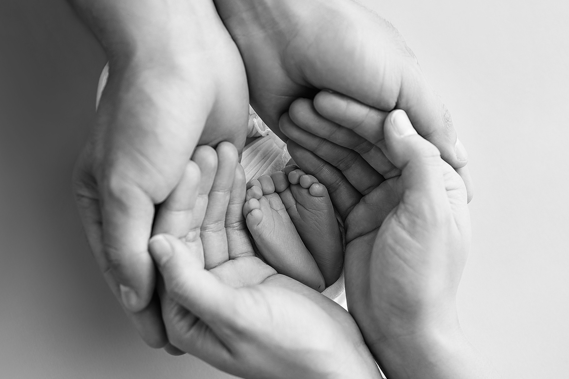 The palms of the father, the mother are holding the foot of the newborn baby. Feet of the newborn on the palms of the parents. Photography of a child's toes, heels and feet. Black and white macro.